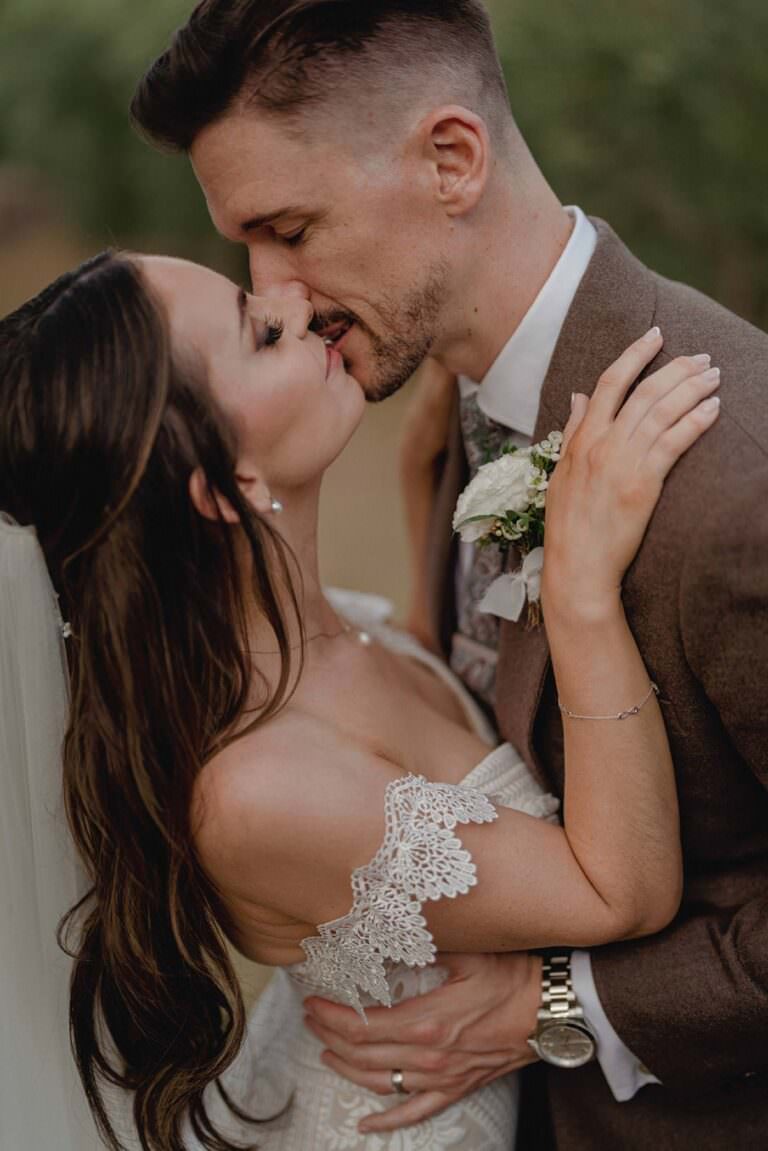 Amid the enchanting backdrop of a wedding at Casa Cornacchi, a bride with long dark hair in a white lace dress leans into her groom, who dons a brown suit. Captured by Federico Pannacchi, their eyes are closed as they savor an intimate moment, her arms tenderly around his neck. Tuscan Wedding Photographer