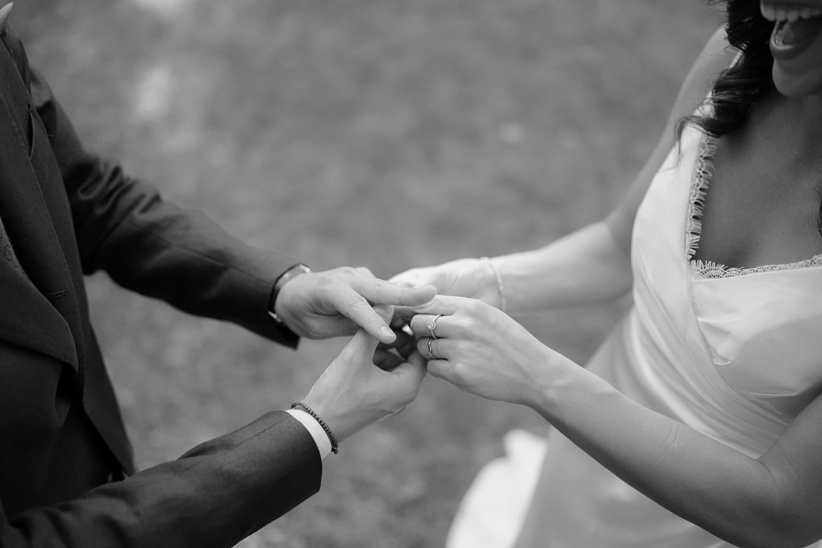 Black and white image of a couple holding hands at their wedding at Tenuta di Monaciano. The bride, with visible curls in a strapless dress, smiles warmly. The groom is in a suit, their faces partially out of frame. Captured by Federico Pannacci, the Tuscan wedding photographer, the background is blurred grass. Tuscan Wedding Photographer