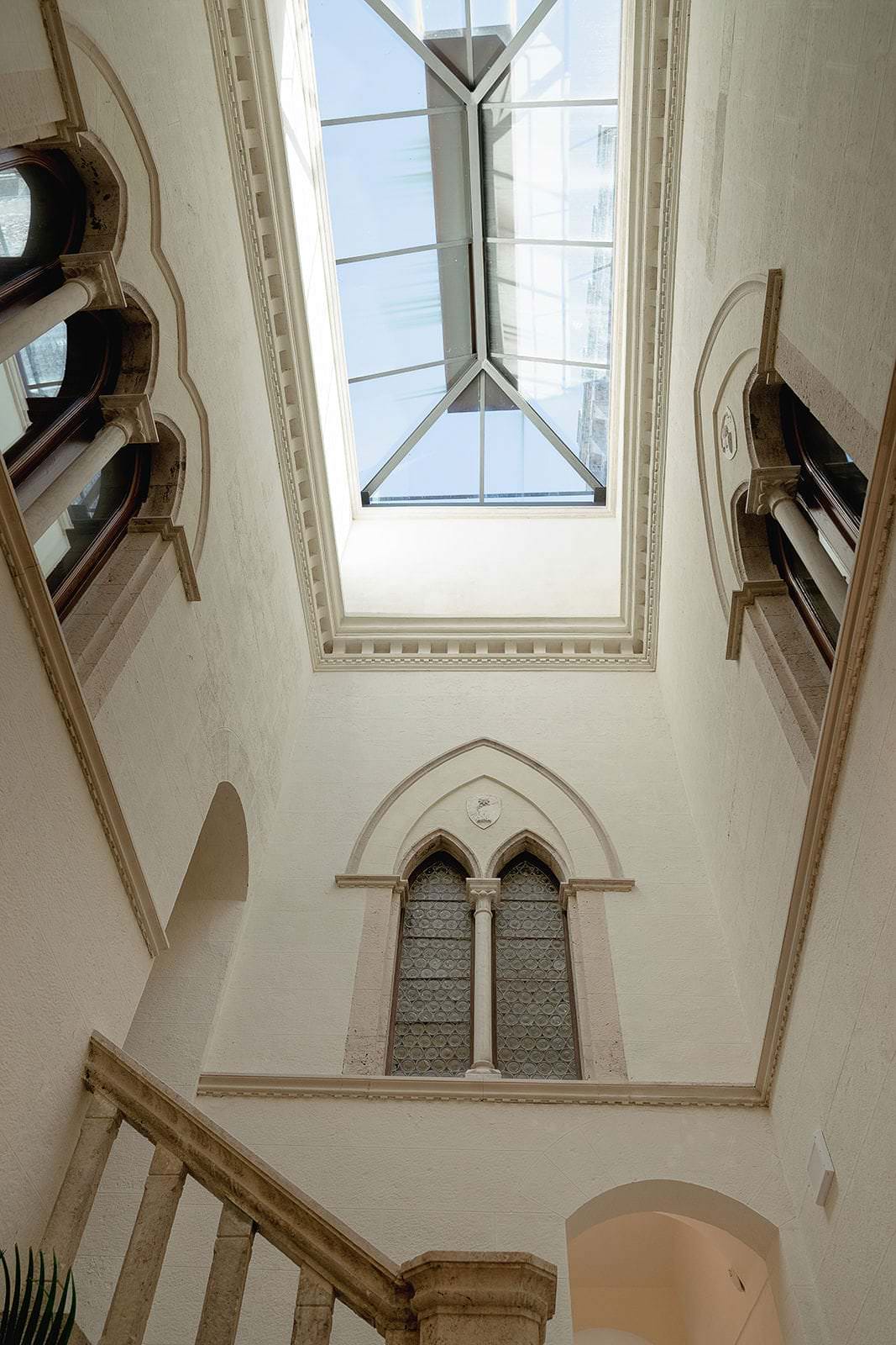 The image captures a bright, airy interior reminiscent of a Tuscan palazzo, with a tall narrow atrium. Arched windows and ornate trim define the space, where Federico Pannacci Photography could capture stunning moments beneath a grand skylight. A carved stone railing graces the foreground. Tuscan Wedding Photographer