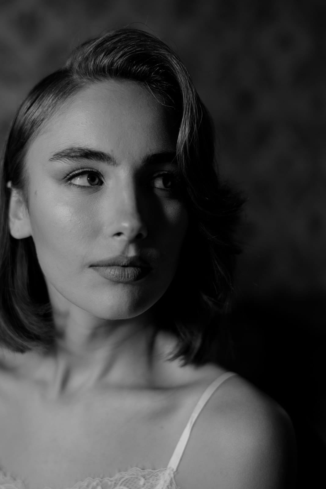 Black and white portrait of a young woman with shoulder-length hair, looking to the side. She has a calm expression and wears a Grace Loves Lace Suki dress with delicate straps. The softly blurred background creates an intimate and moody atmosphere, reminiscent of a serene wedding in Tuscany. Tuscan Wedding Photographer